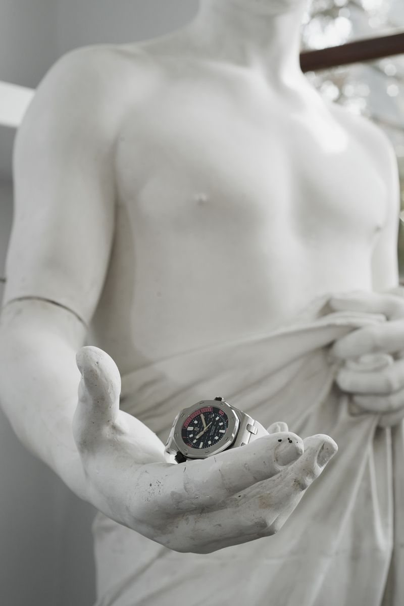 Close-up of a statue holding a luxury wristwatch in its outstretched hand for The Greatest Magazine