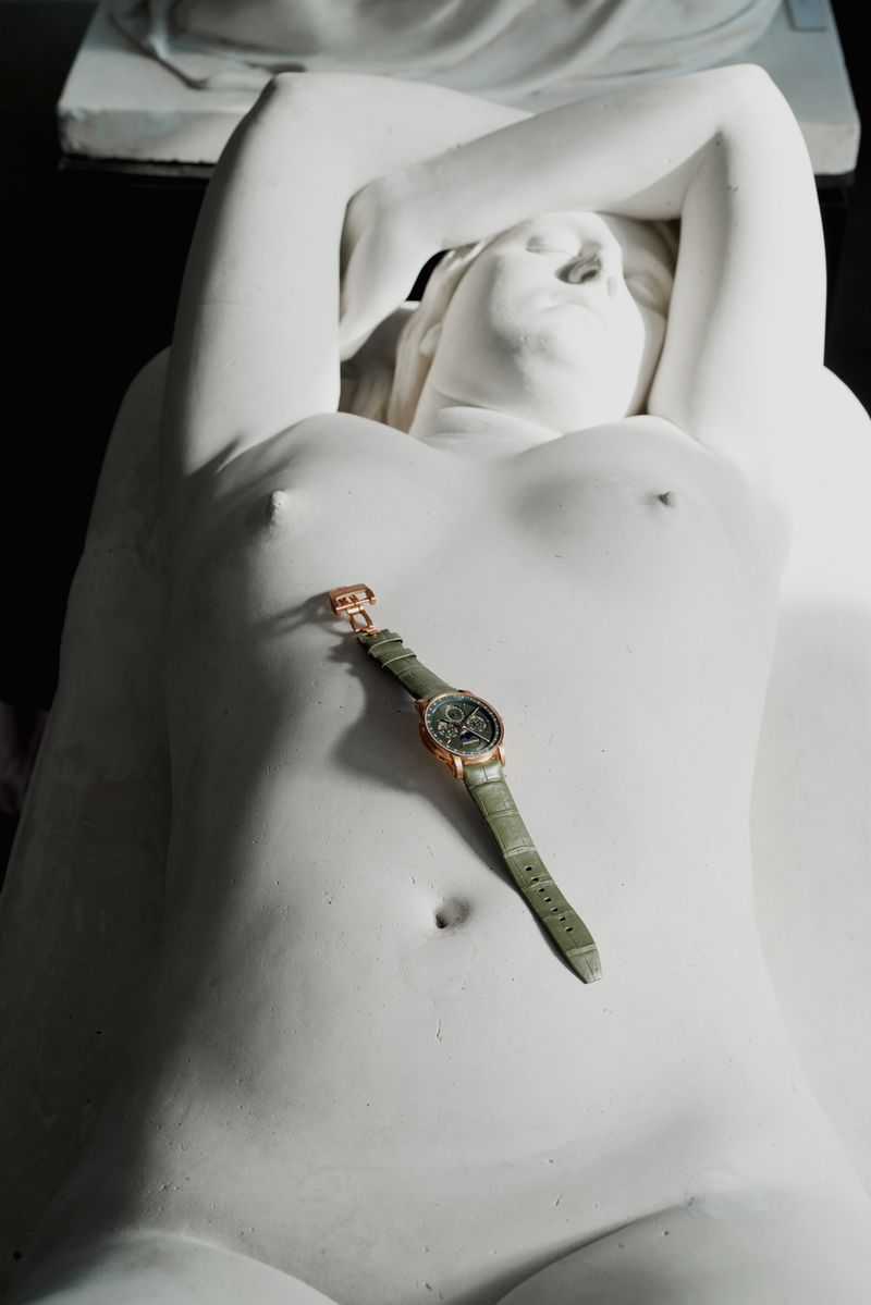 Luxury wristwatch with a green leather strap resting on a white sculptural female form.