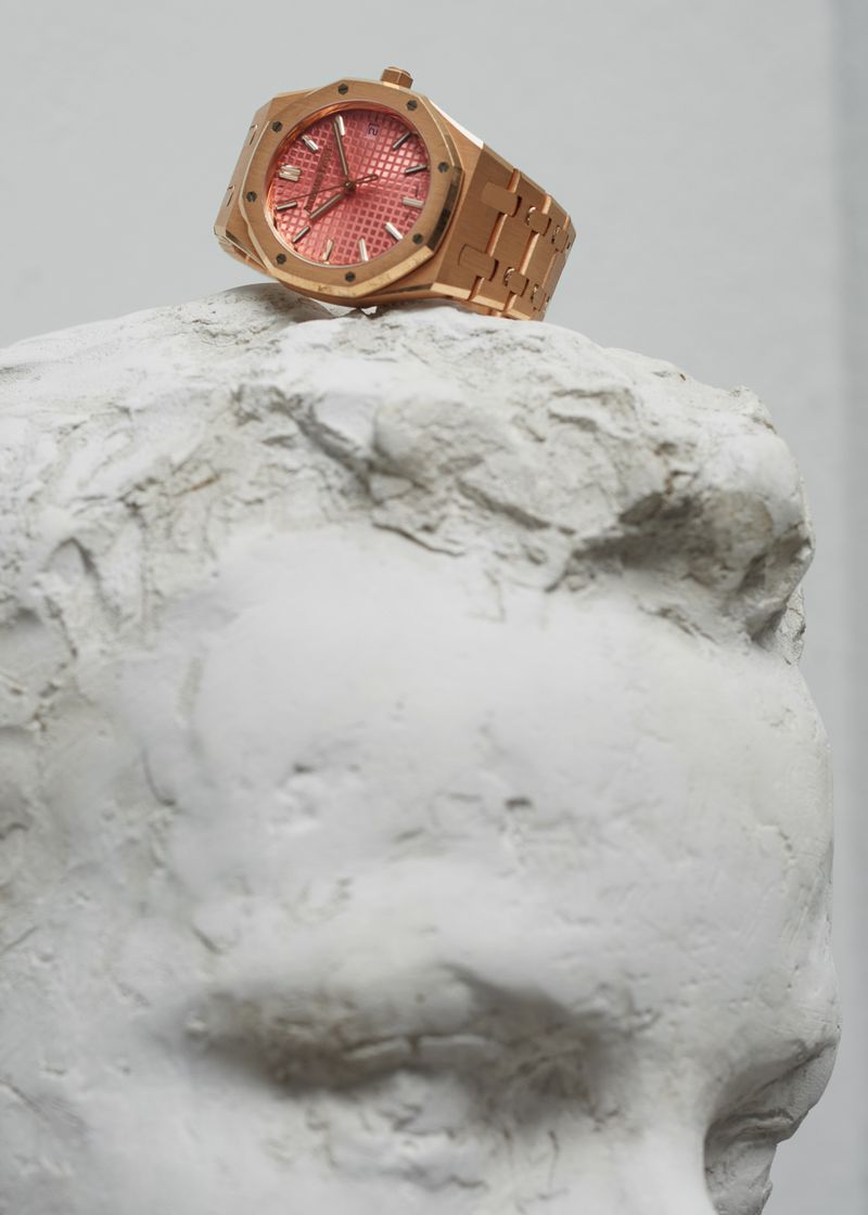 Rose gold luxury watch resting atop a white plaster sculptural bust head in a studio setting.