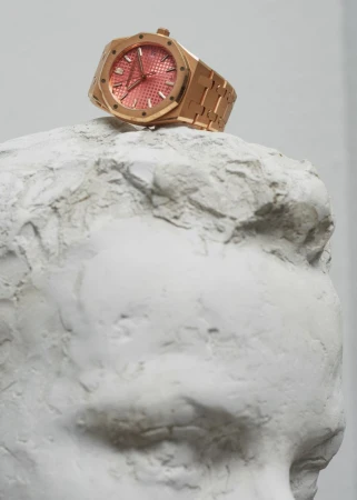 Rose gold luxury watch resting atop a white plaster sculptural bust head in a studio setting.