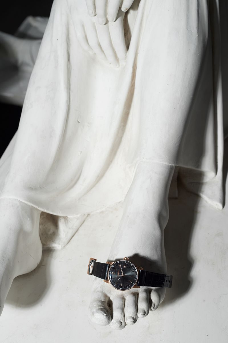 Close-up of a wristwatch placed across the foot of a classical white sculpted statue