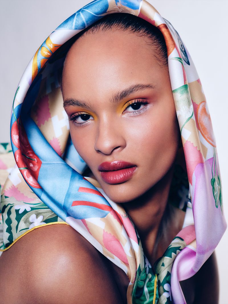 Close-up shot of a Black female with a patterned headscarf, vibrant eyeshadow, and glossy lips in a beauty fashion portrait.