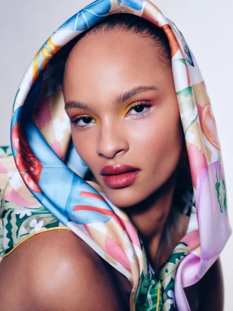 Close-up shot of a Black female with a patterned headscarf, vibrant eyeshadow, and glossy lips in a beauty fashion portrait.