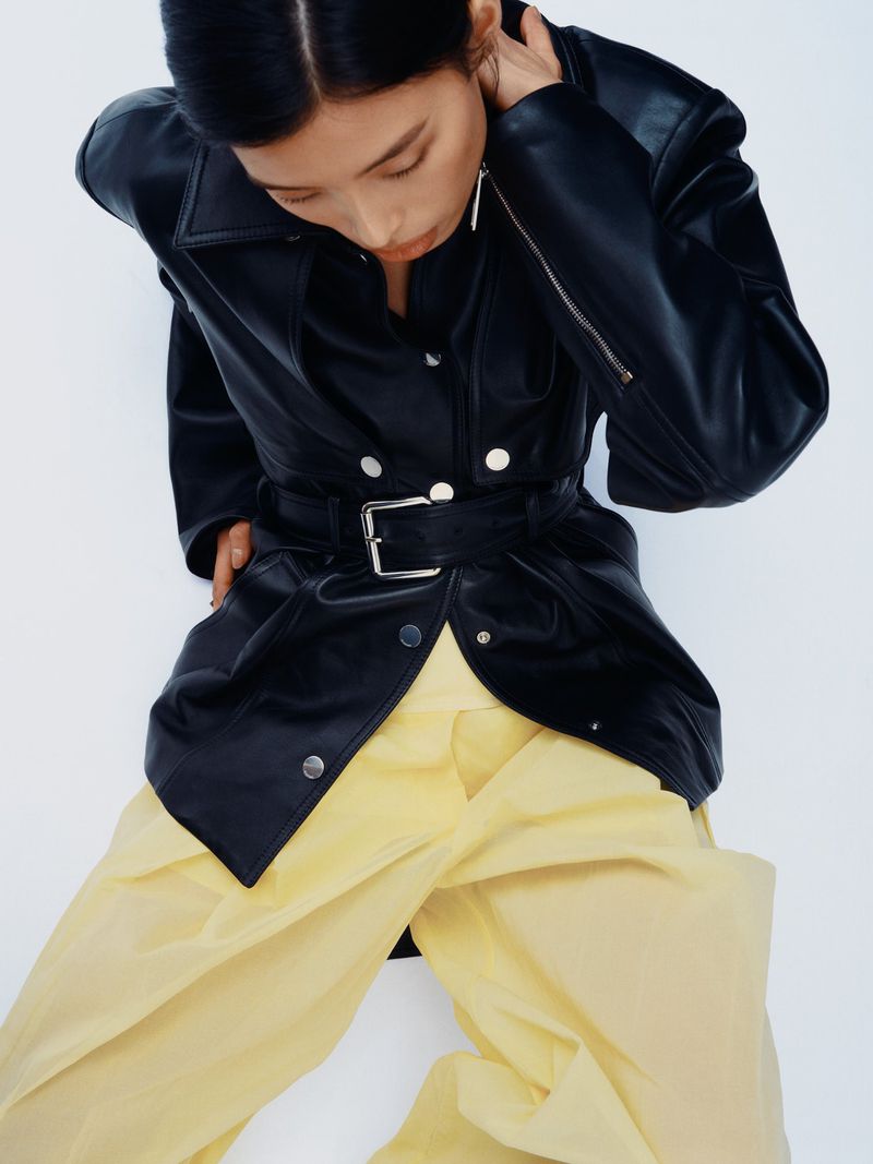 Model in black leather jacket and yellow trousers against a plain white background