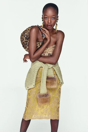 Model in a lace slip dress with a green sweater tied around the waist holding a leopard print handbag against a white background
