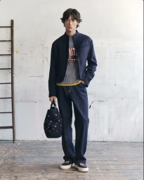 Young male model wearing navy jacket and jeans holding patterned tote bag inside studio