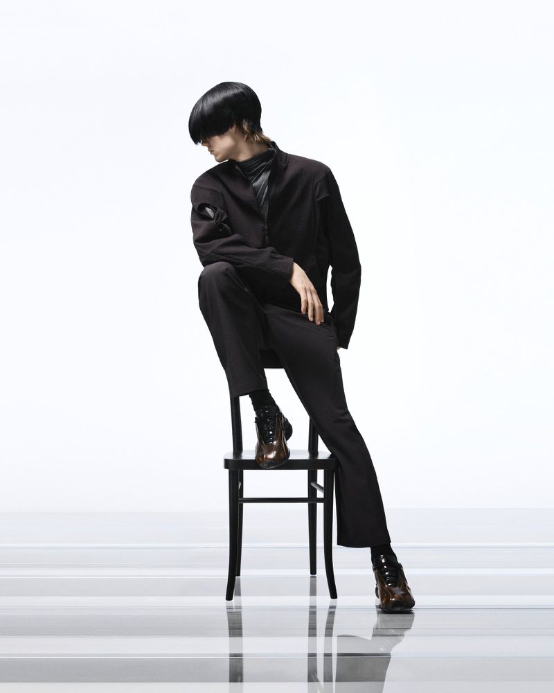 Model in black jacket and trousers seated on a black chair against a bright white background for the Puma project