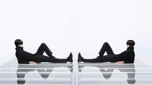 Two models in black outfits lying symmetrically on glass platforms against a plain white background for Puma.