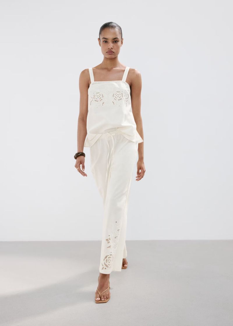 Model in white patterned top and trousers walking against white seamless studio background