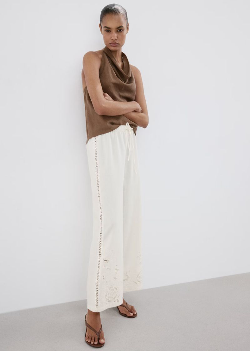 Model standing against a plain white background wearing a brown sleeveless top and white wide-leg trousers