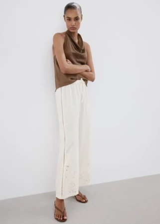 Model standing against a plain white background wearing a brown sleeveless top and white wide-leg trousers