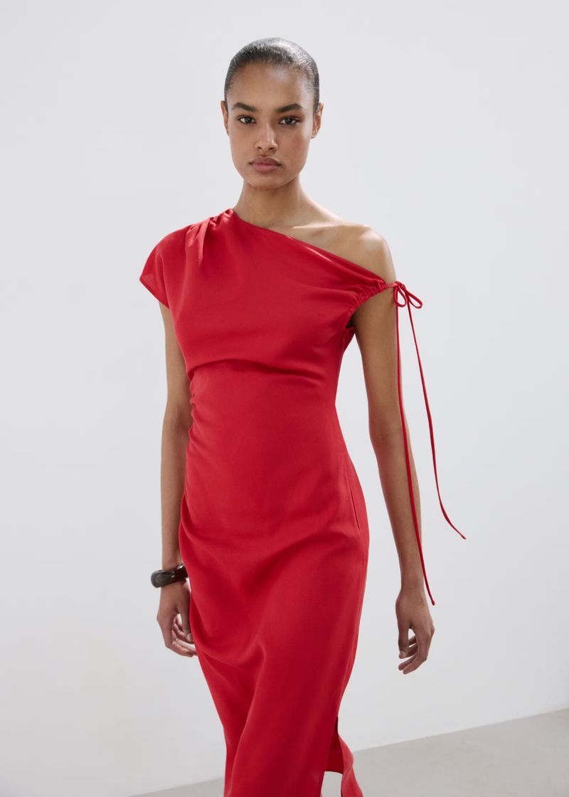 Model Ana Beatriz Cortes wearing an asymmetric red dress against a plain white background for Mango S/S 26
