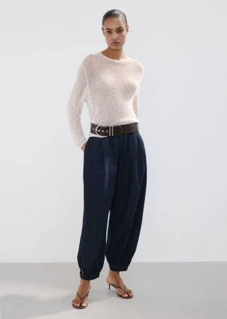 Model Ana Beatriz Cortes wearing a white textured top, dark trousers, and a wide belt against a neutral studio backdrop.