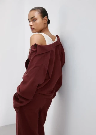 Model wearing a burgundy jacket and matching trousers leaning against a white studio wall
