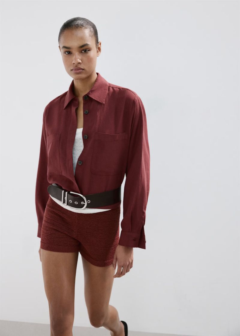 Model wearing a burgundy button-down shirt and shorts with a wide belt against a white backdrop for Mango S/S 26