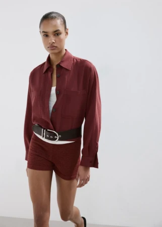 Model wearing a burgundy button-down shirt and shorts with a wide belt against a white backdrop for Mango S/S 26