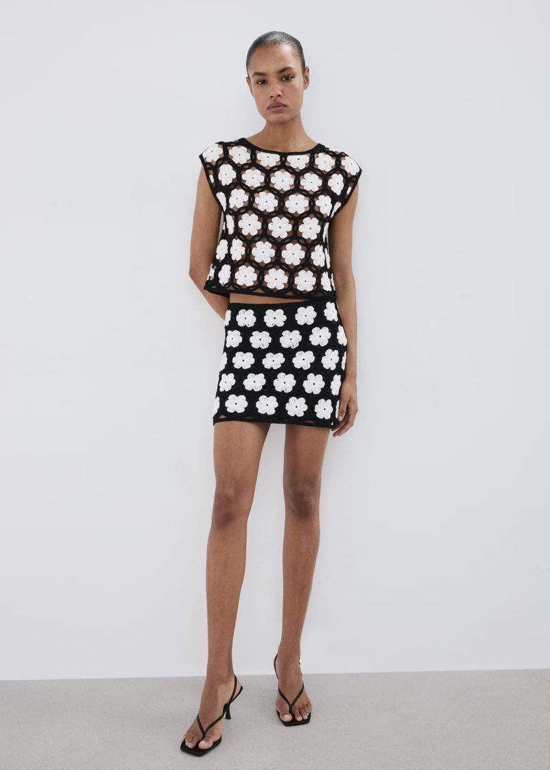 Model wearing a black and white floral crochet top and matching skirt against a minimalist white studio background.