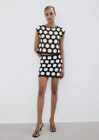 Model wearing a black and white floral crochet top and matching skirt against a minimalist white studio background.