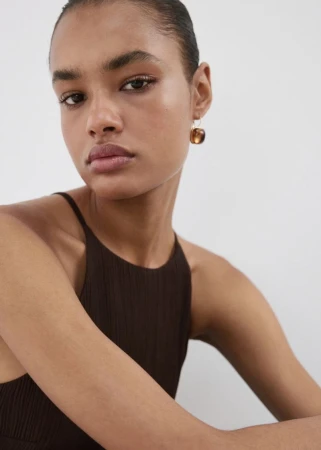 Close up portrait of model wearing brown sleeveless top and resin drop earrings against a white background