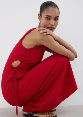 Model wearing a vibrant red sleeveless maxi dress crouching against a plain white studio backdrop.