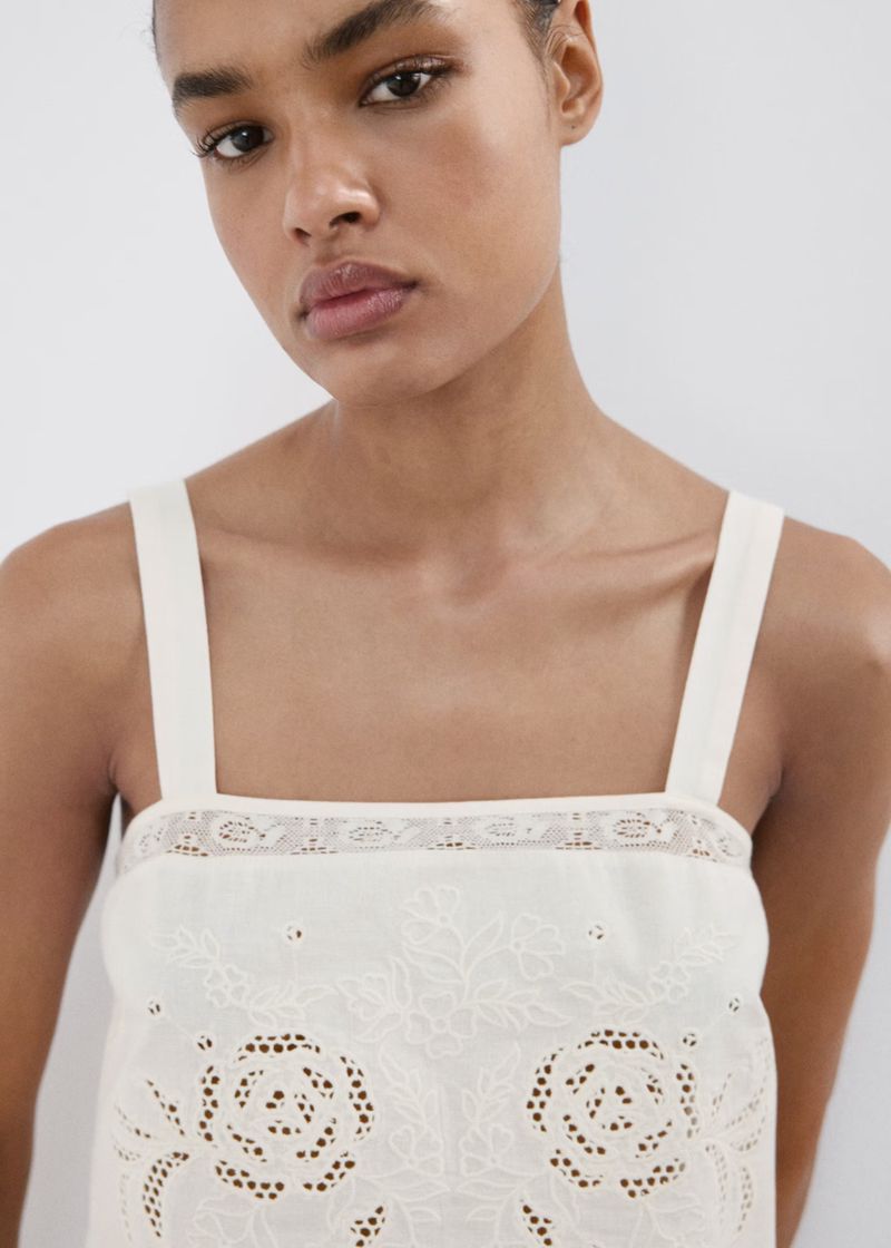 Close-up portrait of a model wearing a white embroidered top with lace trim against a plain white background for Mango S/S 26