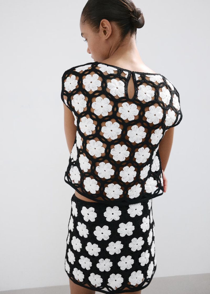 Model wearing a black and white floral crochet top and matching skirt against a plain white studio background.