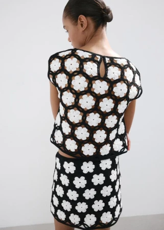 Model wearing a black and white floral crochet top and matching skirt against a plain white studio background.