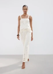 Model in white patterned top and trousers walking against white seamless studio background
