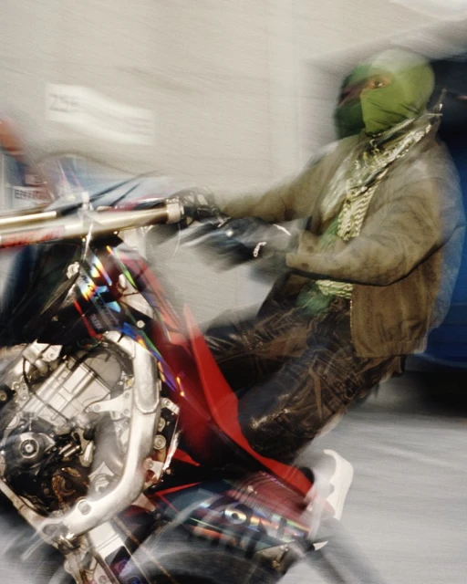 Action shot of an adult riding a motorcycle with a full-face green mask on a blurry background, creating a sense of speed and motion.
