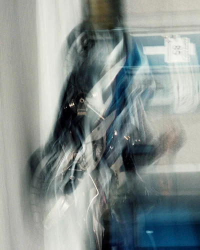 Abstract vertical photograph featuring heavy motion blur over a figure in dark layered clothing with dynamic white and blue streaks.