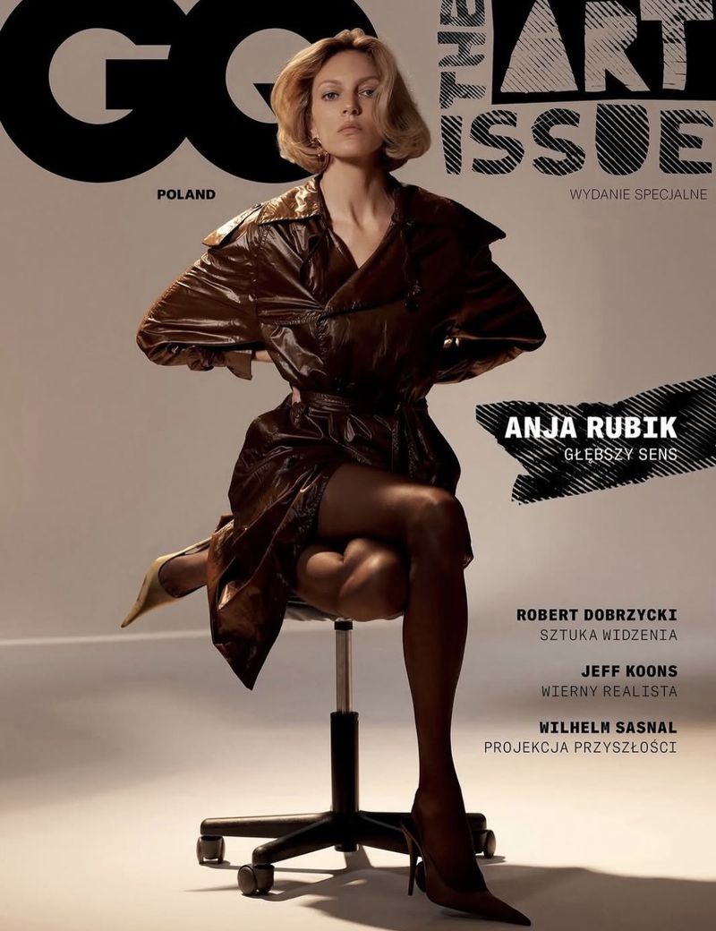 Magazine cover featuring a blonde model in a brown vinyl trench coat, sitting on a rolling chair with heels, against a neutral background.