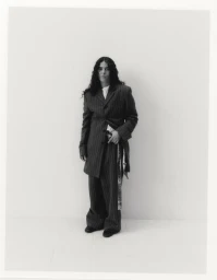 Portrait of 070 Shake wearing a pinstripe oversized suit and patterned belt against white seamless background
