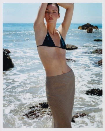 Model Beau_se Genç wearing a dark bikini top and a beige skirt posing by the ocean