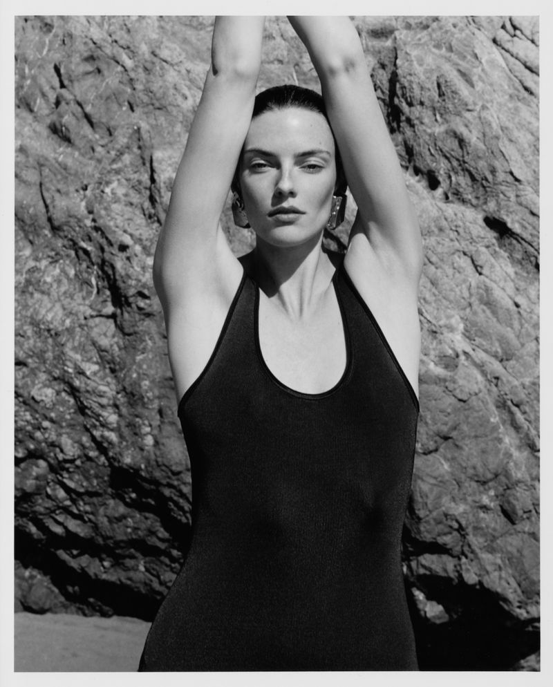 Model with arms raised posing against a rocky coastal backdrop for Revolve