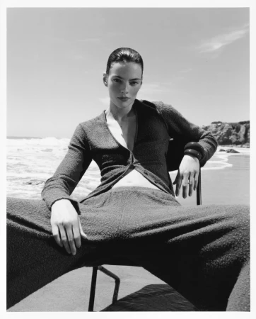 Model seated on a beach chair wearing textured knitwear against an ocean background for Revolve by Agata Serge.