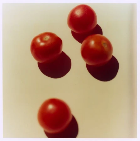 Four red cherry tomatoes arranged on a plain off-white surface with distinct hard shadows cast beneath each one.