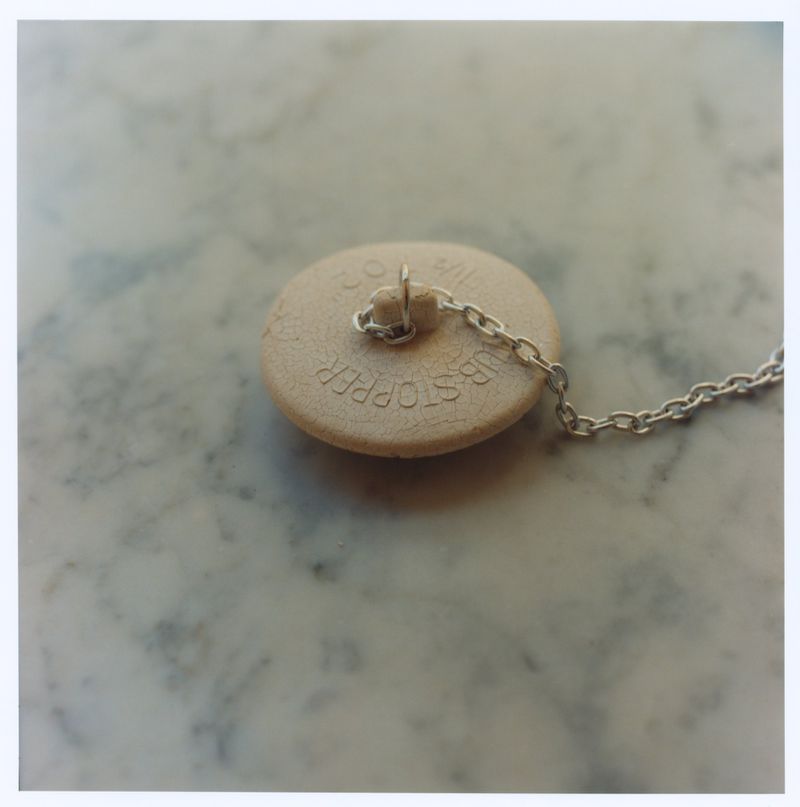 Round beige tub stopper with attached silver chain resting on a pale marble surface