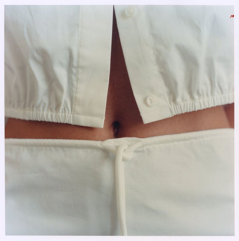 Close-up of a person wearing a white button-down crop shirt and matching drawstring trousers, showing midriff.