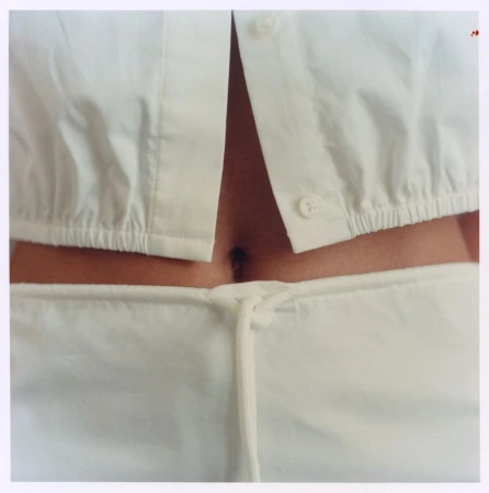 Close-up of a person wearing a white button-down crop shirt and matching drawstring trousers, showing midriff.