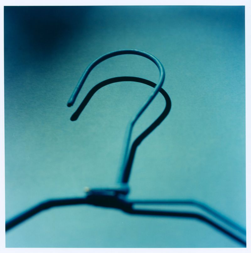 Close-up of a blue wire clothes hanger hook casting a dark shadow against a monochrome background.