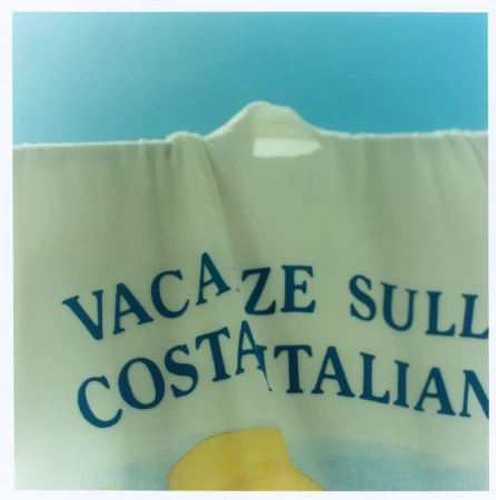 Close up of cream fabric with blue text reading VACAZE SULL COSTA ITALIAN against a blue background.