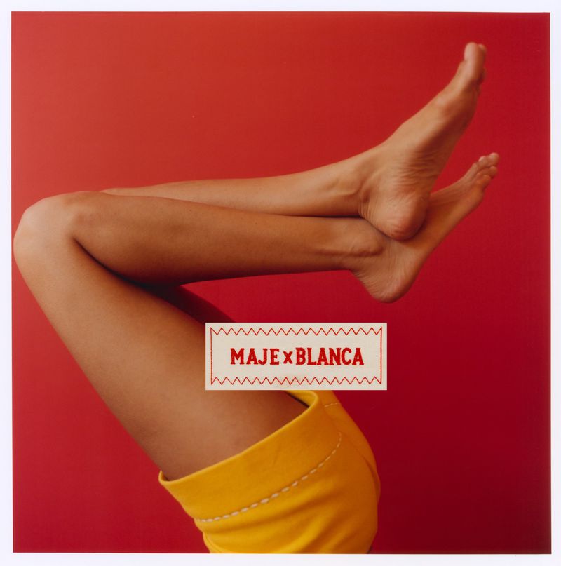 Close-up of bare legs and yellow shorts against a solid red background with a central white label featuring text
