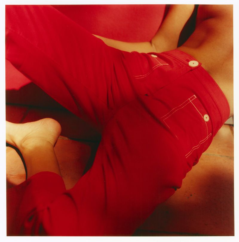 Close-up of a person wearing vibrant red trousers with white buttons reclining against a warm red interior setting.