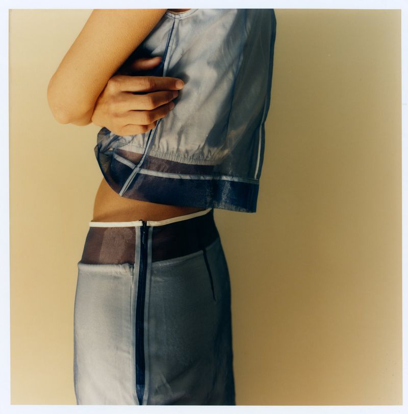 Close-up profile of a woman wearing a sheer blue matching top and skirt set against a neutral studio backdrop.