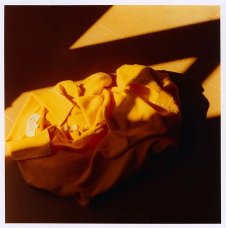 Bright yellow polo shirt resting on a dark surface under dramatic hard sunlight and shadows