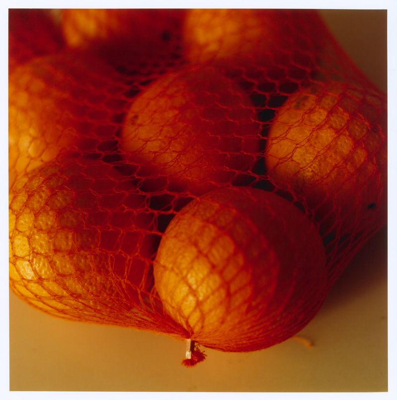 Close-up of fresh round citrus fruit packed inside a bright red mesh produce bag against a plain background