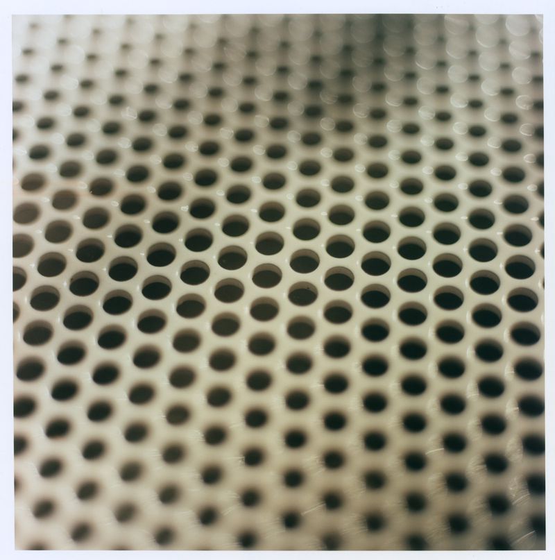 Close-up of a perforated metal surface featuring an offset repeating grid of circular holes against a neutral tone.