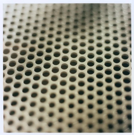 Close-up of a perforated metal surface featuring an offset repeating grid of circular holes against a neutral tone.