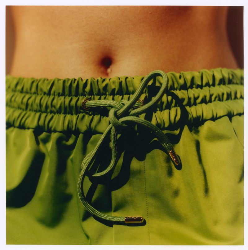 Close-up of olive green drawstring shorts with a tied waist and exposed midriff photographed by Martin Gatti for Maje x Blanca Miro.