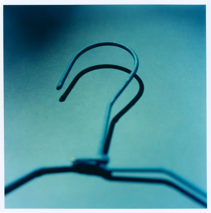 Close-up of a blue wire clothes hanger hook casting a dark shadow against a monochrome background.